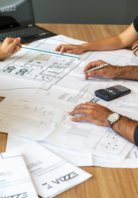 Blueprints on a table with multiple people's hands visible looking them over.