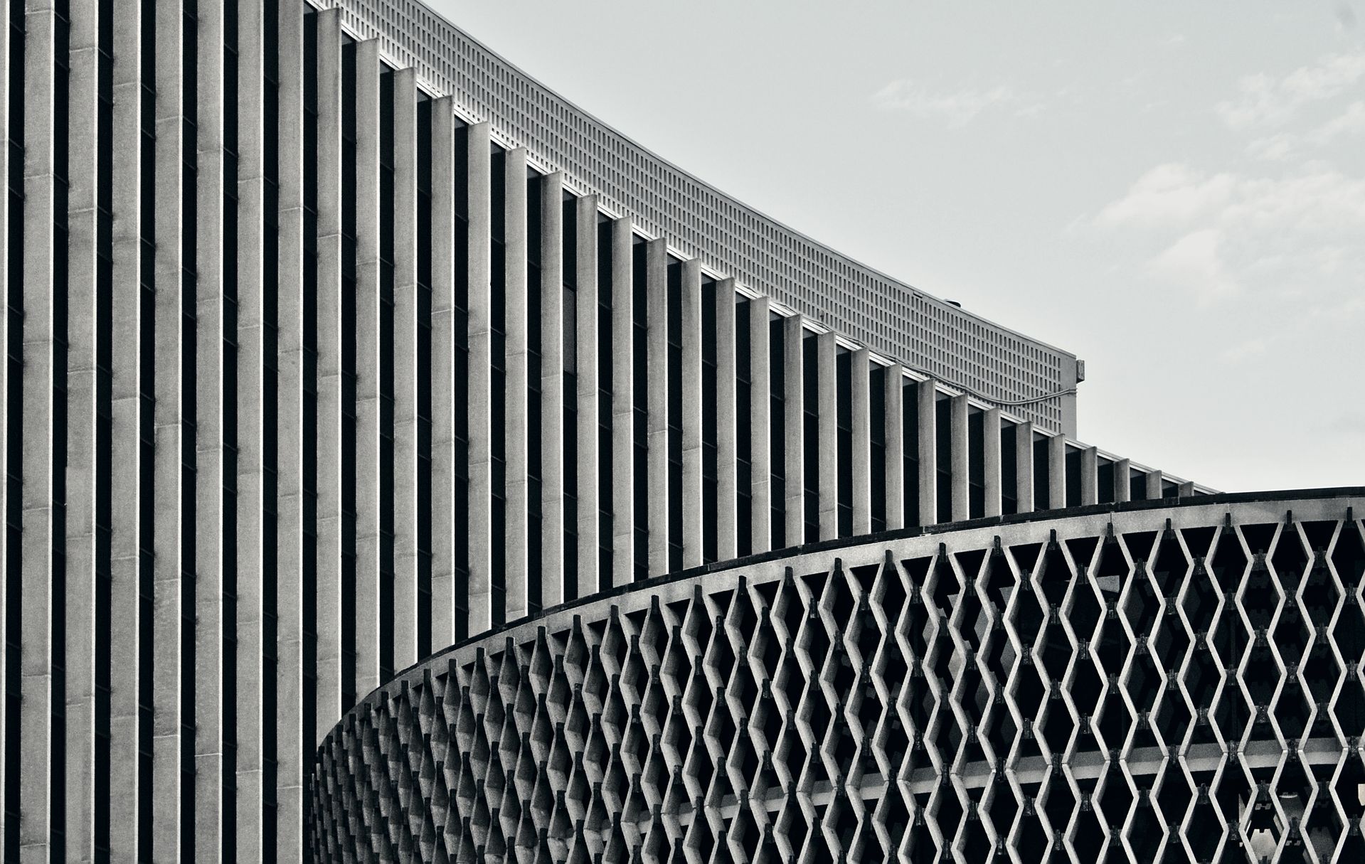 Modern building facade with vertical white striped panels above geometric patterned mesh in black and white
