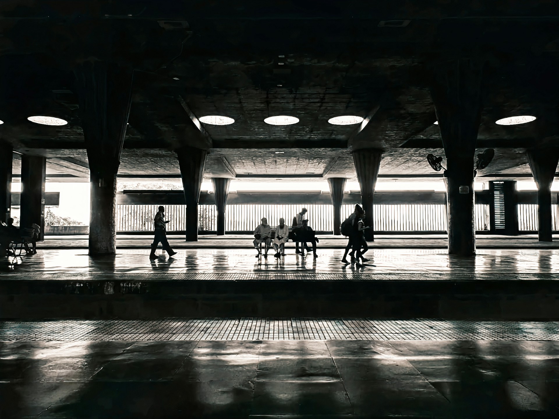 Silhouettes of people waiting in a dimly lit train station with bright windows