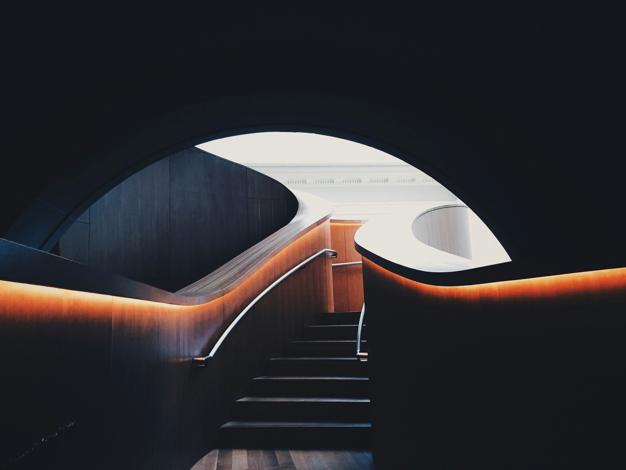 Underground staircase with dark lighting showing a glimpse of outside.